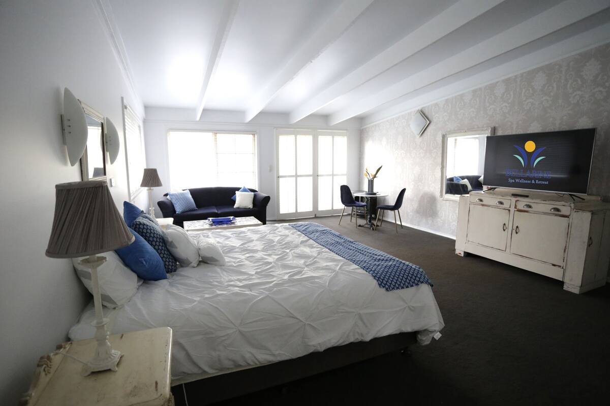 A bedroom with a bed, bedside table, lamp, dresser, TV, and a chair.