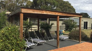 A covered outdoor seating area with lounge chairs and a brick pathway. - Bellarine Spa Wellness & Retreat (Portarlington)