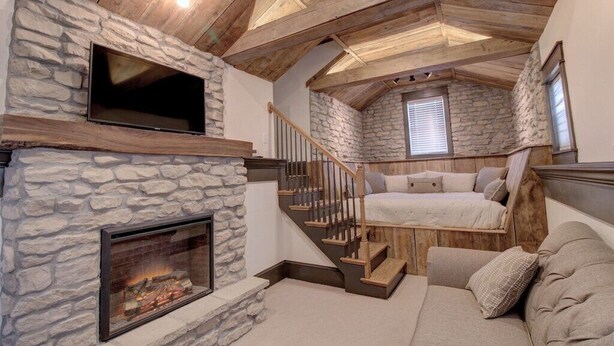 A cozy attic bedroom with a stone fireplace, a bed, and a TV mounted on the wall. - The St. Charles Guest House, lovely historic home, fun for families and groups (St. Charles)