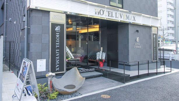 A modern hotel with a glass facade, a prominent entrance, and a sign reading "HOTEL L'VEMAX".