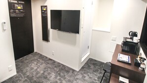 A hotel room with a flat-screen TV mounted on the wall, a desk with a coffee maker, and a small chair.