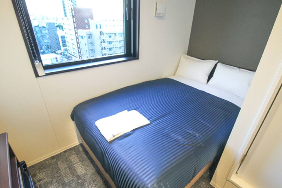 A hotel room with a bed, a window, and a carpeted floor.
