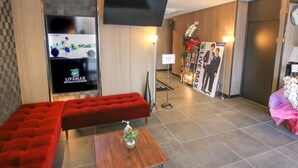 A modern hotel lobby with a red sofa, a flat-screen TV, and a reception desk.