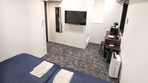 A hotel room with a bed, a desk, a chair, a flat-screen TV, and an air conditioning unit.
