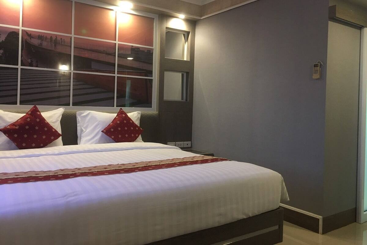 Une chambre d’hôtel avec un grand lit, une fenêtre donnant sur la ville, une table de chevet et un téléphone fixé au mur.
