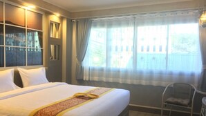 A hotel room with a large bed, a chair, and a window with curtains. - Grand Visanu Hotel (Nakhon Sawan)