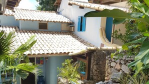 A courtyard with stone walls, potted plants, and a tiled roof. - Tudo Azul Internacional (Búzios)