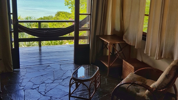 A room with a view of the sea, a hammock, a chair, and a small table. - Tudo Azul Internacional (Búzios)