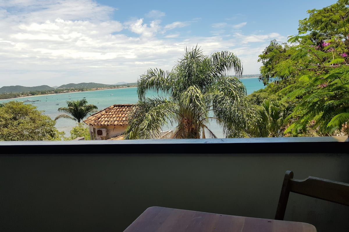 A view from a balcony overlooking a coastal area with a small building, palm trees, and a clear sky.