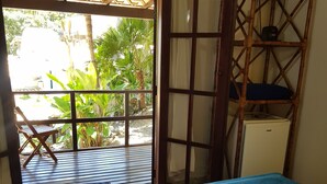 A room with a bed, a wooden chair, a small table, and a view of greenery outside. - Tudo Azul Internacional (Búzios)