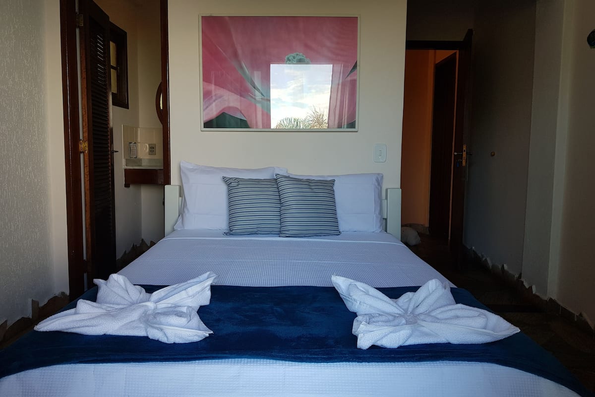 A neatly made bed with white and striped pillows, a blue blanket, and two towels arranged on the bed.