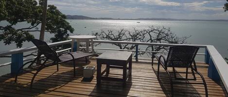 A wooden deck with outdoor furniture, overlooking a body of water and distant land.