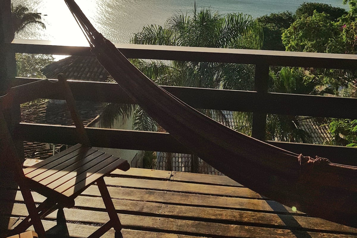 A wooden deck with a hammock and chairs overlooking a body of water and distant land.