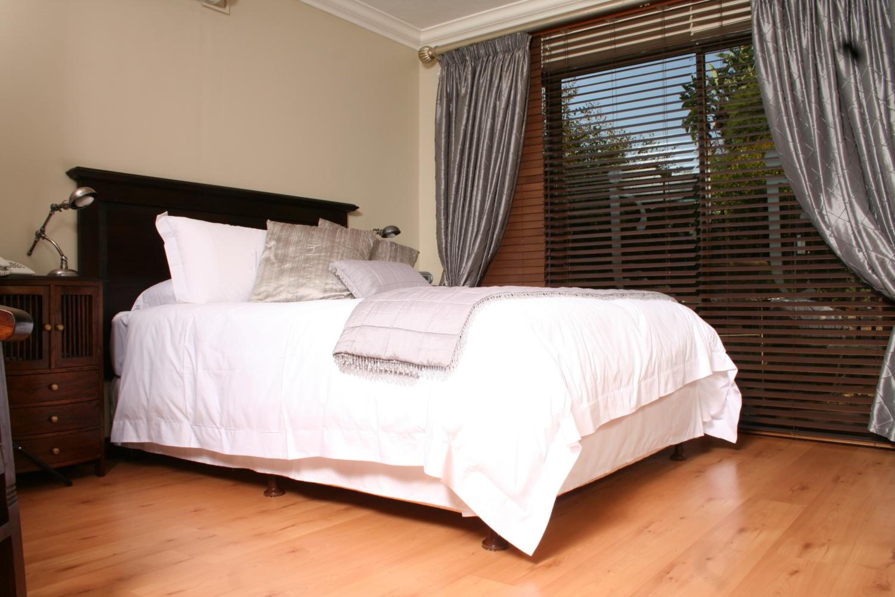 A neatly made bed with white linens, a wooden headboard, and a bedside table with a lamp.