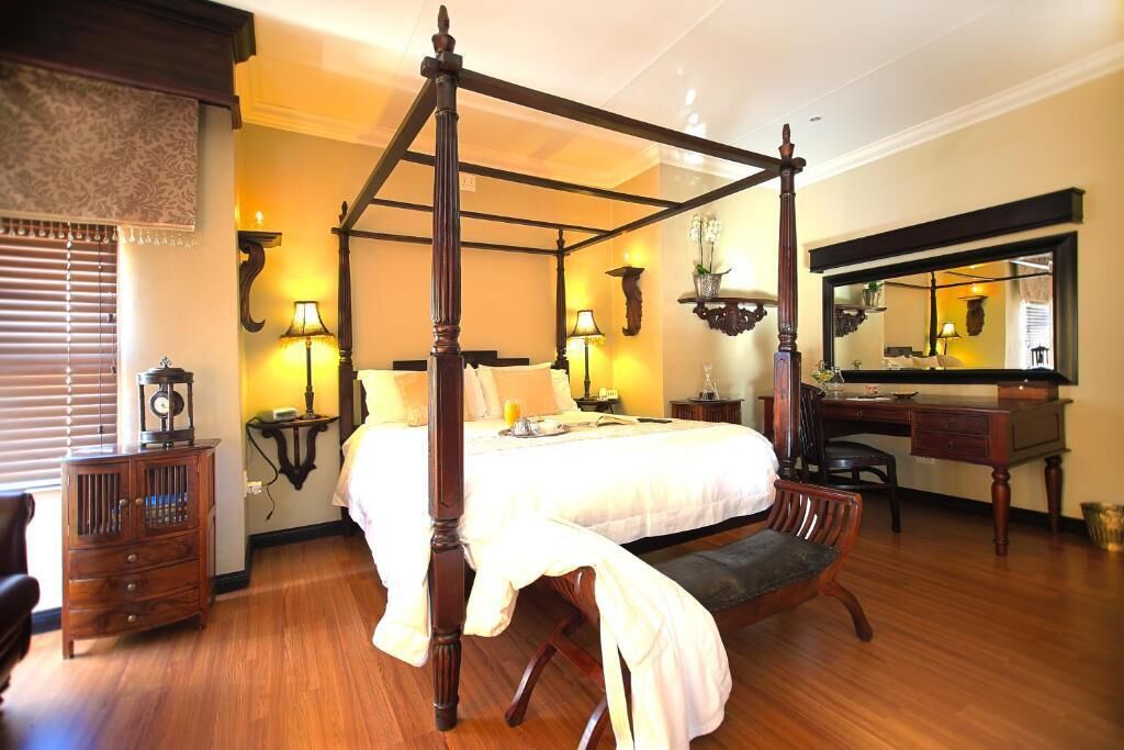 A four-poster bed in a hotel room with a desk, chair, and mirror.