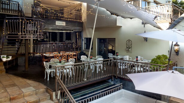 Un restaurante de varios niveles con mesas al aire libre, una escalera y luces colgantes.