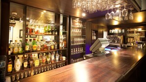 Zona de bar con estantes llenos de botellas de licor, una caja registradora y copas de vino colgando.