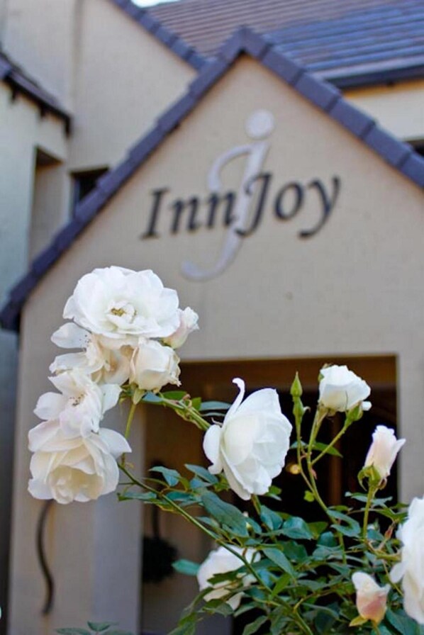 Un edificio con el cartel "InnJoy" y rosas blancas en primer plano.