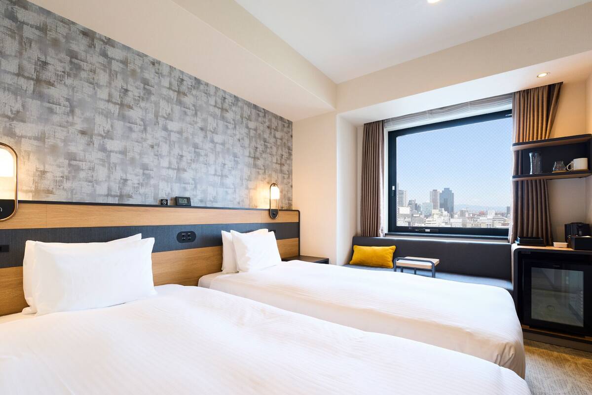 A hotel room with two beds, a city view, a small table, and a TV.