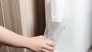 A hand holding a glass of water from a white water dispenser with the brand name 'Coway' visible on the side.