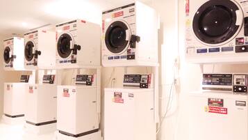 A row of white laundry machines with control panels and labels in a commercial setting.
