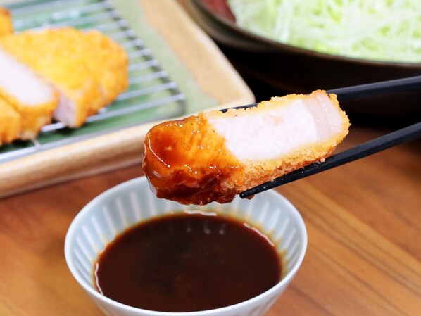A piece of breaded and fried food held by chopsticks over a small bowl of dark sauce.