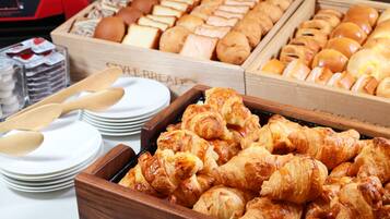 A buffet with various baked goods including bread, rolls, and pastries.