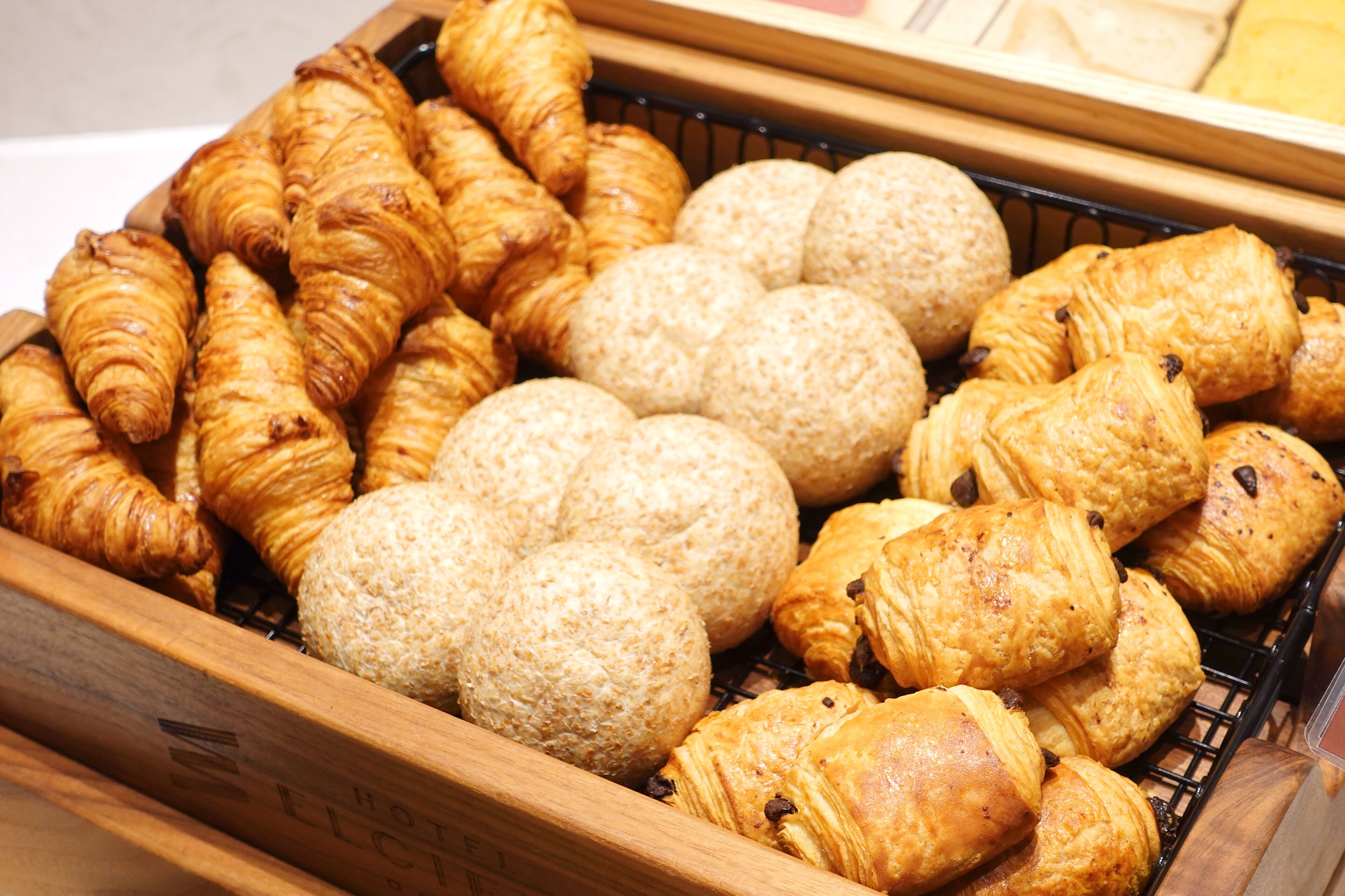 A wooden tray filled with various types of pastries, including croissants and bread rolls.