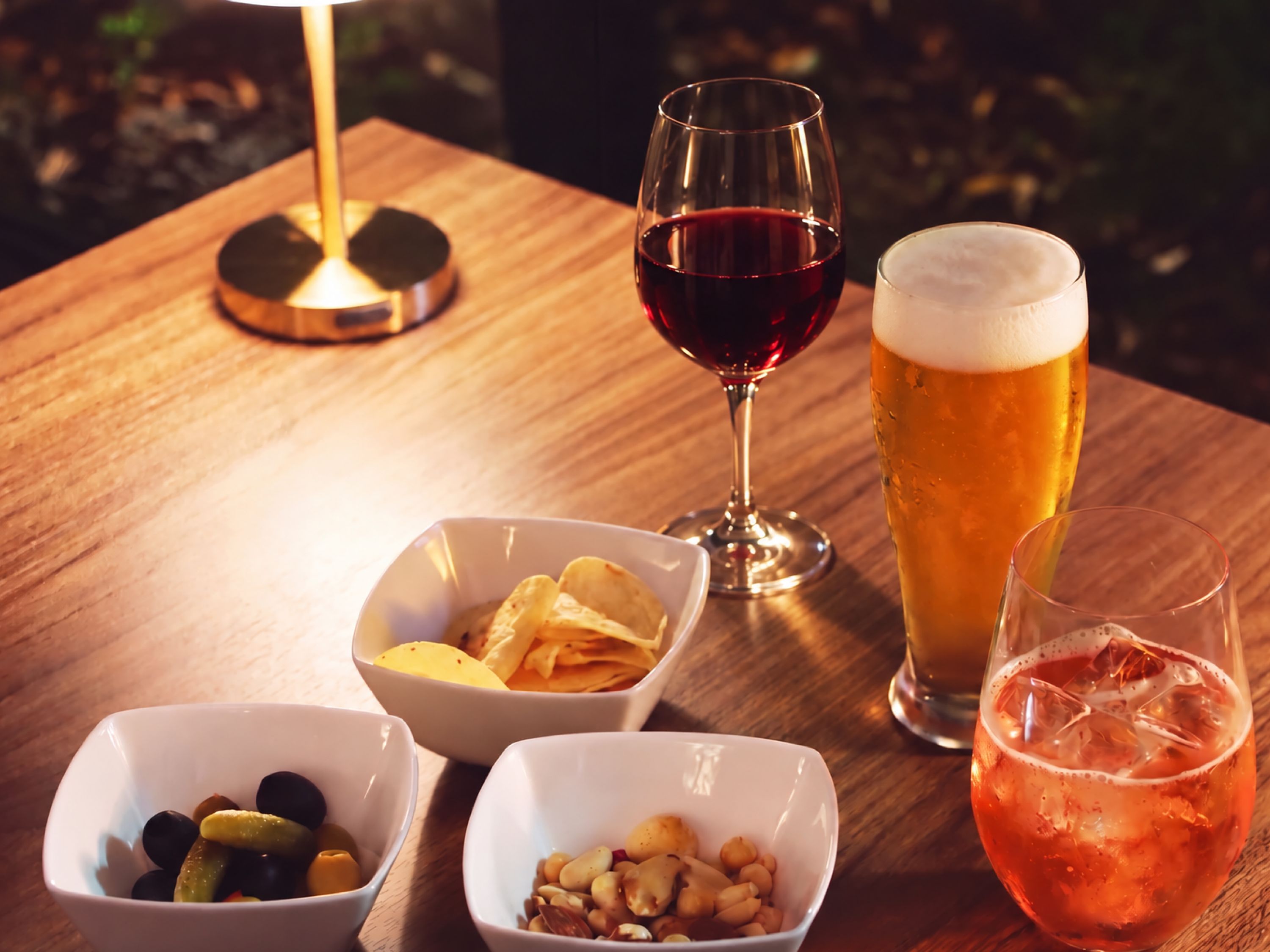 Una mesa de madera con una copa de vino, una jarra de cerveza y cuencos de aperitivos.