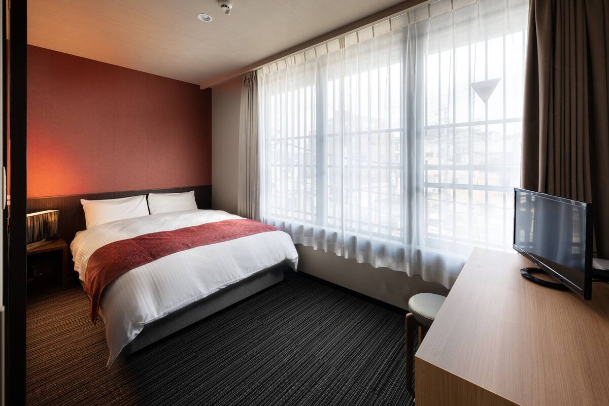 A hotel room with a bed, a desk, a television, and a window with curtains.