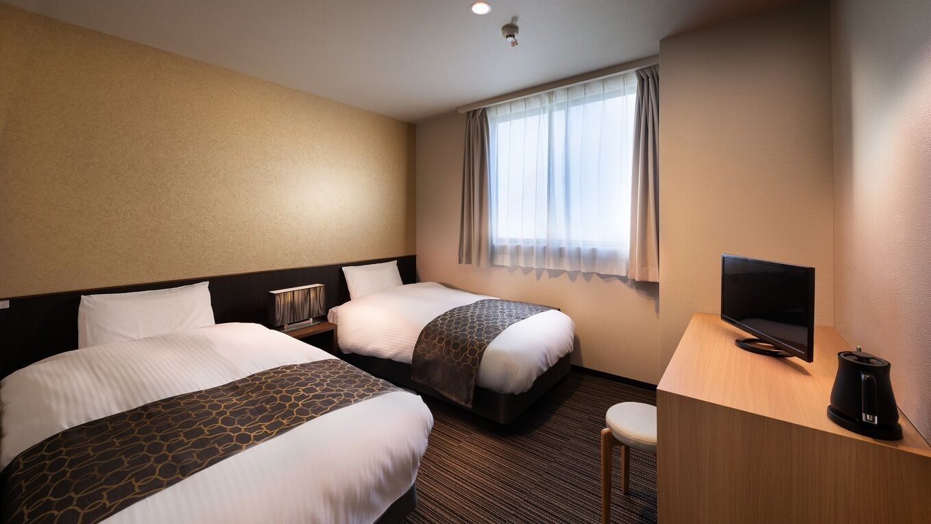 Ein Hotelzimmer mit zwei Betten, einem Fernseher, einer Kaffeemaschine und einem Fenster mit Vorhängen.