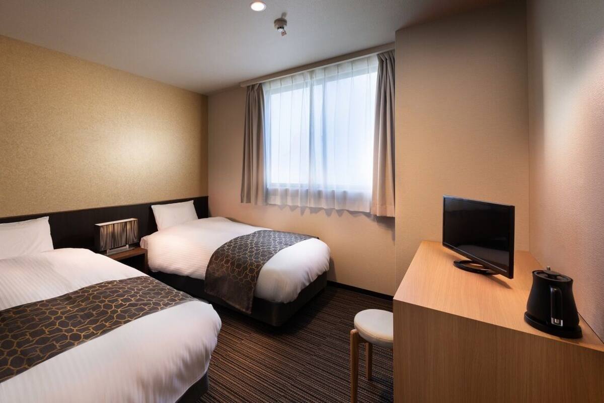A hotel room with two beds, a TV, a coffee maker, and a window with curtains.