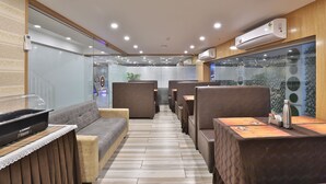 A modern restaurant with booth seating, wooden flooring, and an air conditioning unit on the wall. - Hotel Le Grand (Surat)