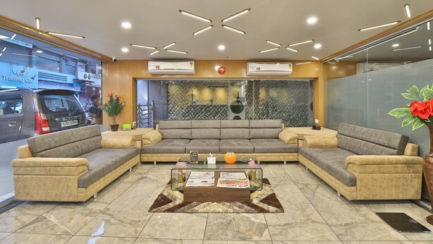 A modern lobby with a sectional sofa, a glass coffee table, and a decorative rug. - Hotel Le Grand (Surat)