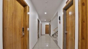 A hallway with wooden doors, a tiled floor, and a staircase with a handrail. - Hotel Le Grand (Surat)