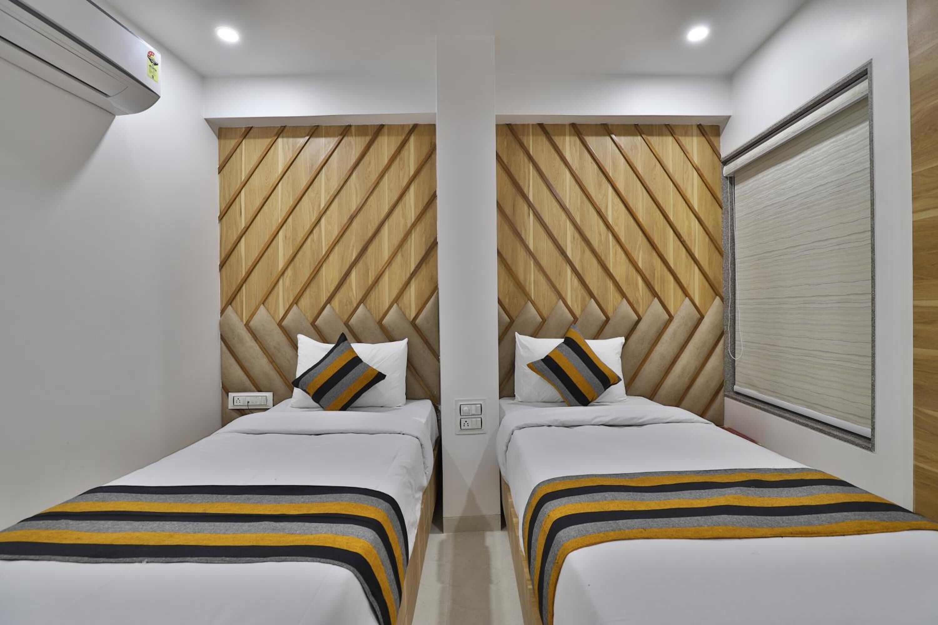 Une chambre d’hôtel avec deux lits, des têtes de lit en bois, du linge de lit blanc et une fenêtre avec des stores.