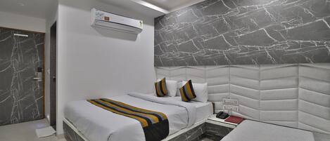 A modern bedroom with a marble-patterned headboard, a bed with white bedding and decorative pillows, and an air conditioning unit on the wall.
