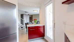 A modern kitchen with a built-in refrigerator, a red cabinet, and a window providing natural light. - La Closerie des Tremieres by Interhome (Saint Georges de Didonne)