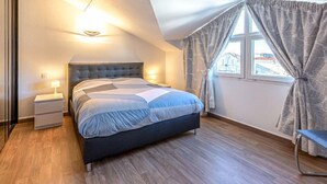 A bedroom with a bed, bedside lamps, a window with curtains, and a view of buildings outside. - La Closerie des Tremieres by Interhome (Saint Georges de Didonne)