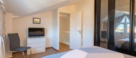 A modern bedroom with a bed, a TV on a dresser, a chair, and a large window with a view.