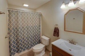 Een badkamer met een douchegordijn met dessin, een toilet, een wastafel met spiegel en een handdoek aan een ring.