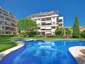 A residential building with a swimming pool, surrounded by greenery and a clear sky.