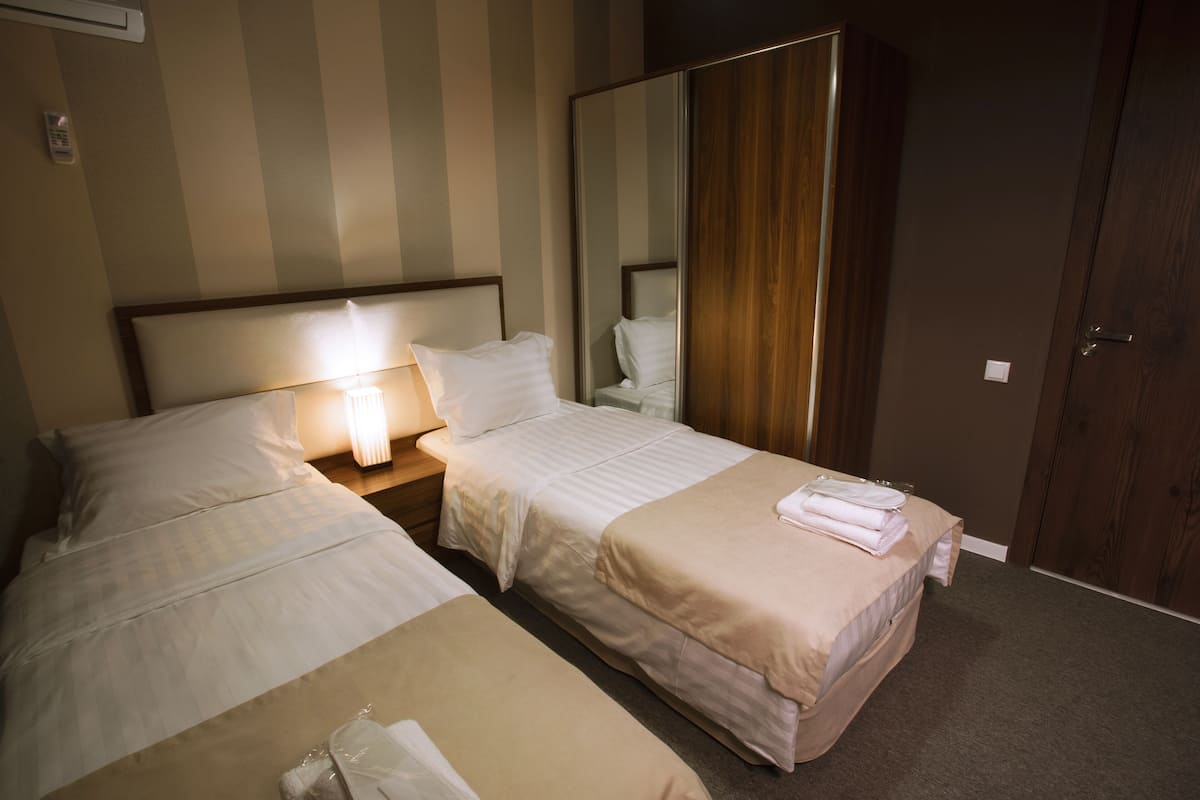 A hotel room with two beds, a wardrobe, a bedside table with a lamp, and a mirror.