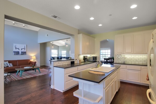 A modern kitchen with white cabinets, a central island, and a dining area with a brown sofa and striped rug.
