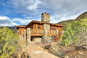 A log cabin with a stone chimney, wooden balcony, and a stone pathway leading to the entrance.