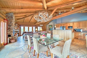 A spacious living area with a glass-top dining table surrounded by wicker chairs, a stone fireplace, and a stone wall.