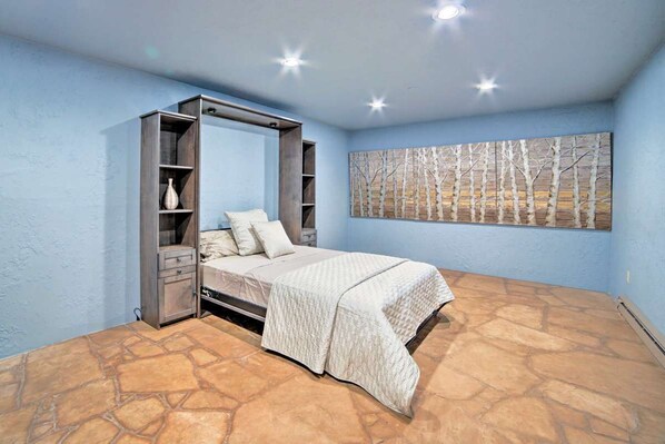 A bedroom with a bed, a wardrobe, a painting, and a stone floor.