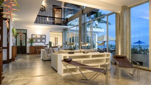A spacious living area with a high ceiling, large windows, and a view of the ocean.