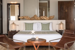 A modern hotel room with a large bed, two bedside tables with lamps, a round coffee table, and two leather chairs. - The Beach House by Reveal (Kamburugamuwa)