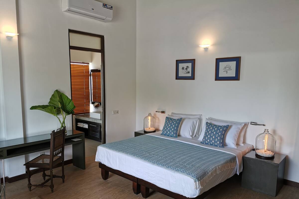 A bedroom with a bed, bedside tables, a desk, a chair, a mirror, and a potted plant.